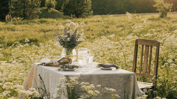 Elegant handmade linen tablecloth and napkins in soft beige, styled with fresh flowers and ceramic plates on a dining table.