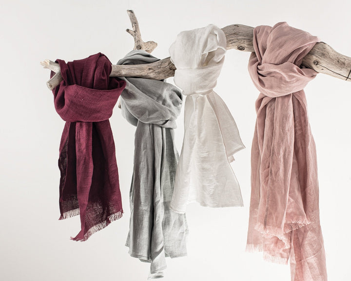 A light beige handmade linen scarf draped elegantly on a wooden hanger, showcasing its soft and breathable texture.